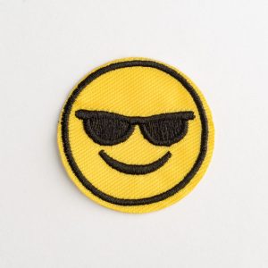 Emoji smile embroidered patch on white background. Cool face with sunglasses. Modern decorative element for clothing.